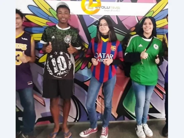 Alunos reunidos diante de um painel colorido na escola.