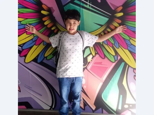 Aluno com os braços abertos diante de um mural de asas coloridas.