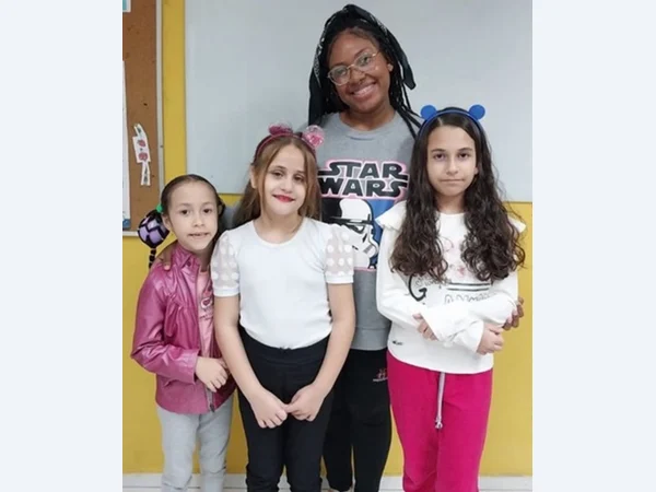 Educadora e três alunas reunidas em sala de aula.